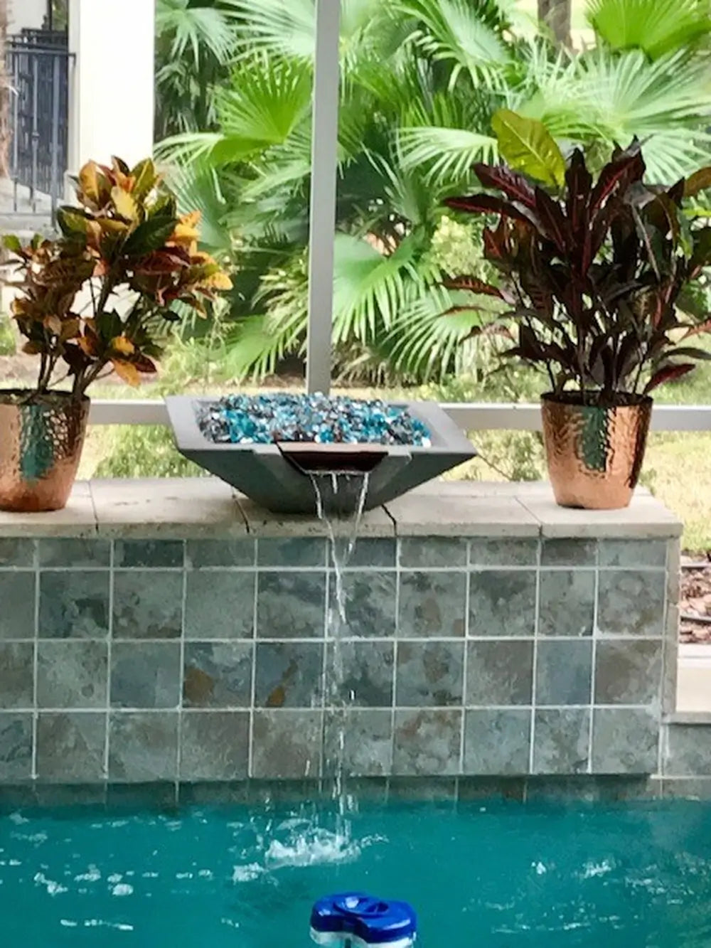 Travertine TessaRai Square Fire/Water Bowl Kit with blue fire glass and waterfall spillway above screened backyard pool