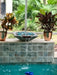 Travertine TessaRai Square Fire/Water Bowl Kit with blue fire glass and waterfall spillway above screened backyard pool
