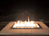 Linear square gas fire pit burner glowing at night with a white stone tile surround and clean modern aesthetic.