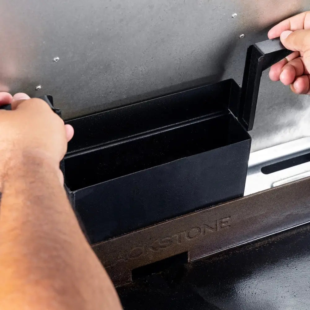 Hands removing rear-mounted grease tray from Blackstone 28-inch drop-in outdoor gas griddle