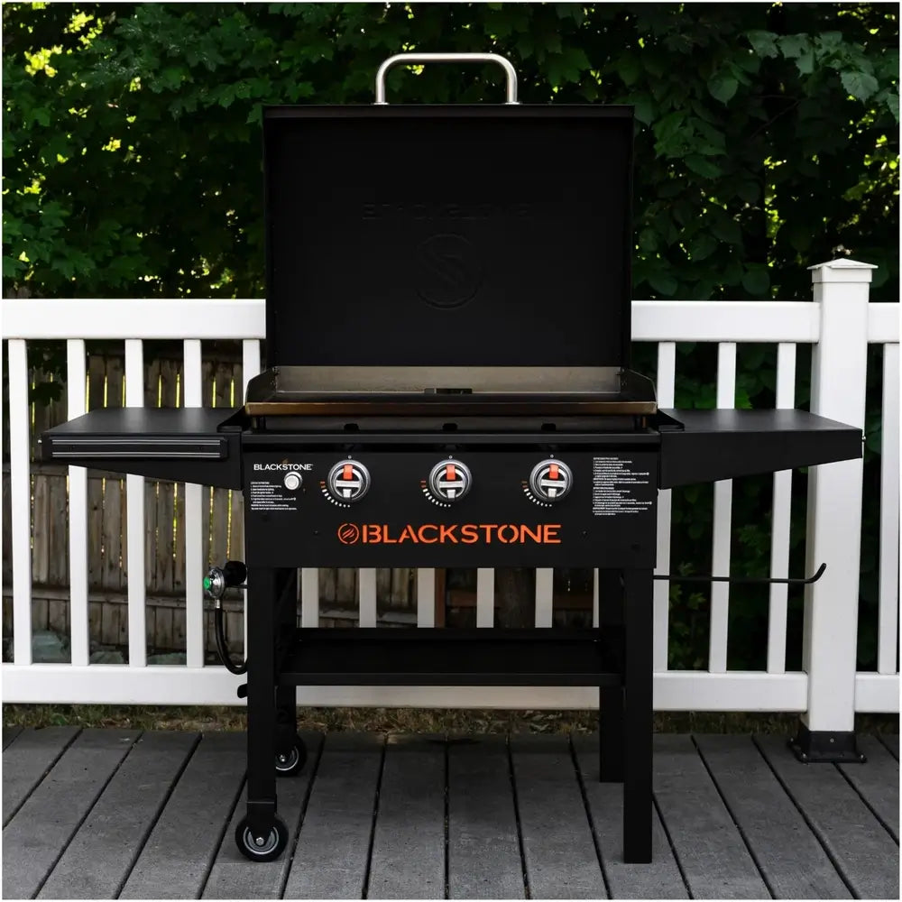 Blackstone 28" griddle with hood set up on deck with open lid and triple burner controls in view