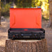 Blackstone 20"x14" portable camping griddle with bright orange hood open, set on a tree stump in the forest, ideal for outdoor cooking.