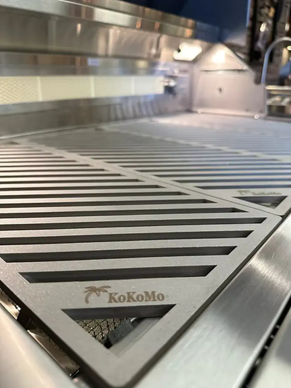 Extreme close-up of the KoKoMo LuxCut laser-cut cooking grate with its diagonal pattern and the KoKoMo logo etched into the corner.