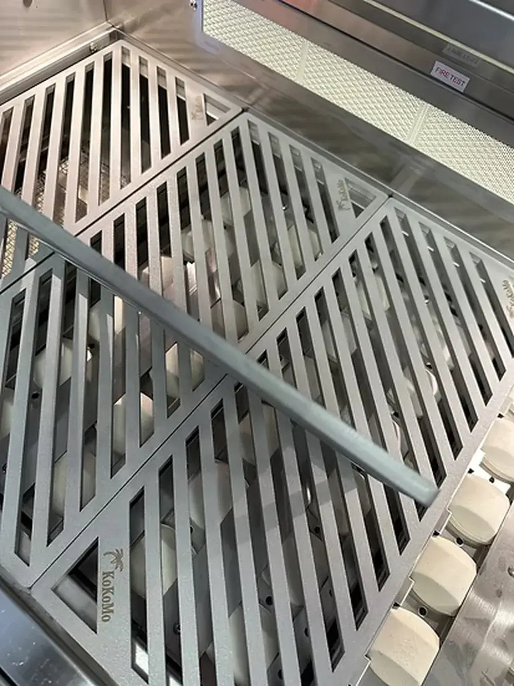 Overhead view of the four-section KoKoMo LuxCut laser-cut cooking grate with one section being lifted, showing the ceramic briquettes below.