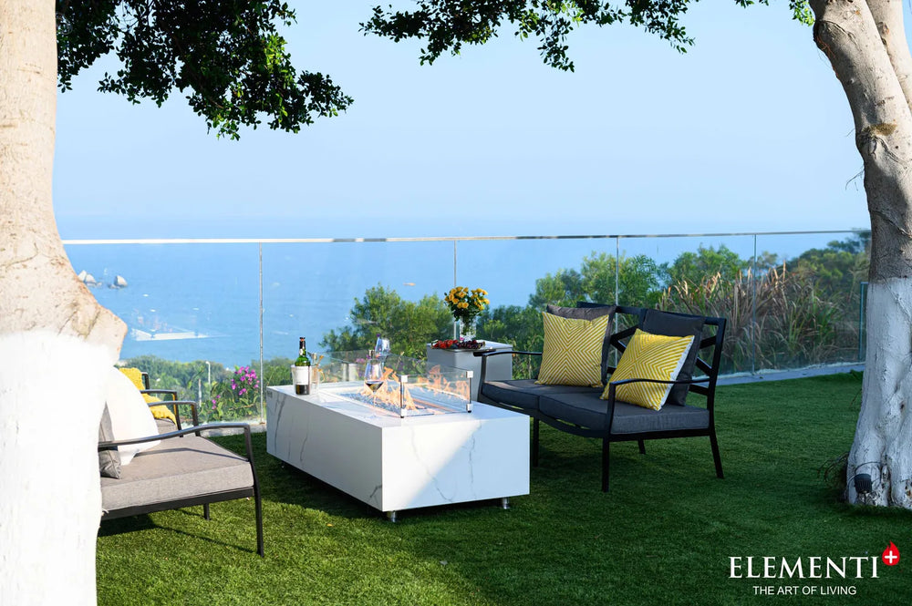 Functional detail of the Carrara Bianco fire table used as an outdoor coffee table, with the matching lid covered and styled with wine, champagne, and snacks.