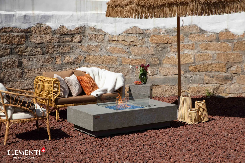 Elementi Plus Monte Carlo 60-inch fire table in light gray with blue fire glass and patio seating.