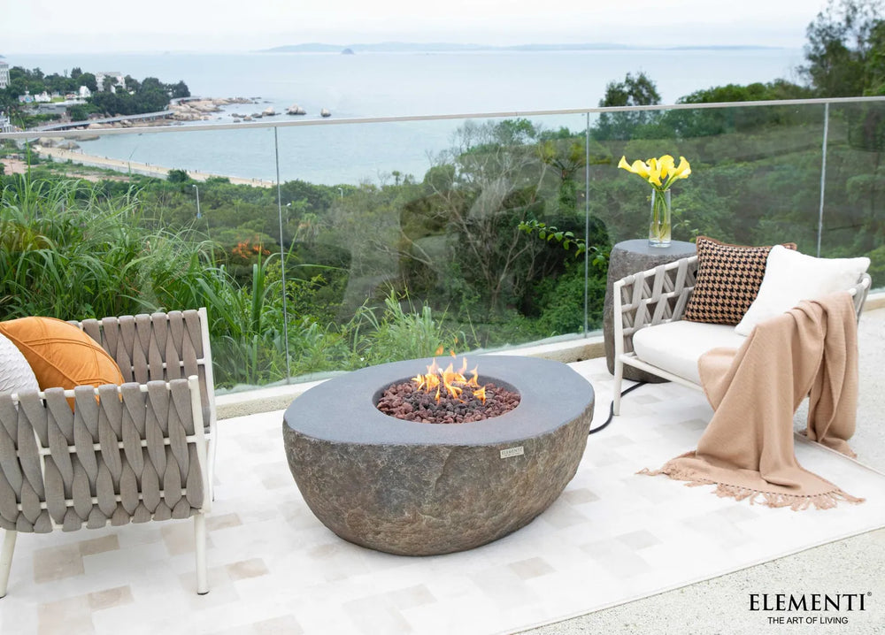 The Elementi Boulder fire table integrated into a modern balcony lounge area with a sweeping ocean view.