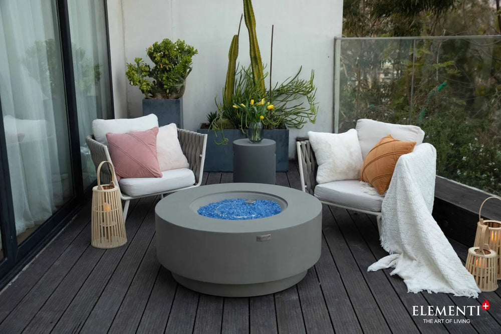 Elementi Plus Colosseo light gray fire table with blue fire glass in outdoor lounge setting.