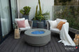 Elementi Plus Colosseo light gray fire table with blue fire glass in outdoor lounge setting.