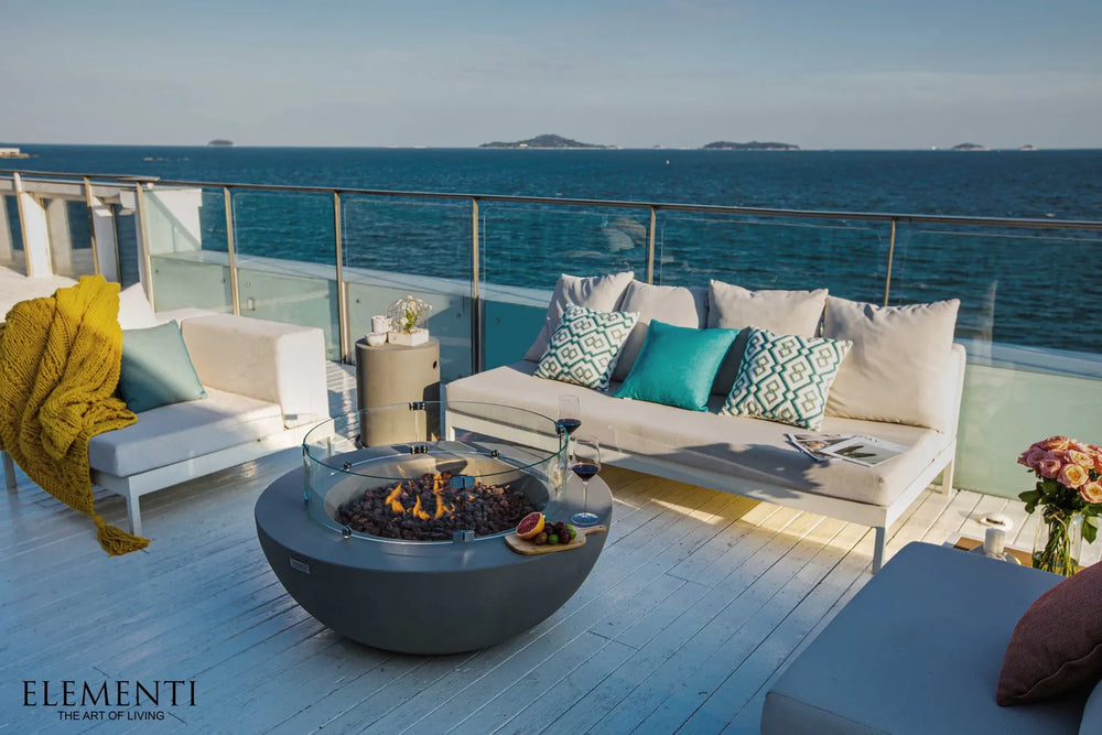 Elementi fire table on a beachfront wooden deck with turquoise pillows and ocean views.