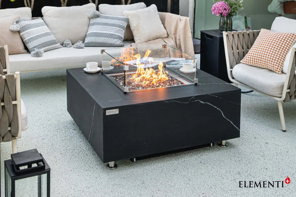 Close-up of the Bulgaria Black fire table’s linear burner, highlighting the clear glass wind guard and shimmering bronze fire glass under a warm flame.