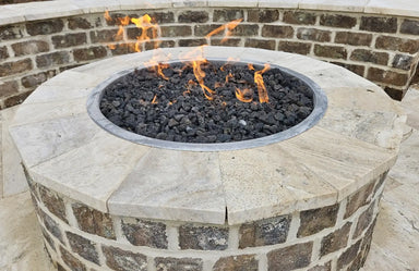 Round gas fire pit featuring a light-colored Travertine TessaRai GFRC capstone with lava rocks and a natural stone masonry base.