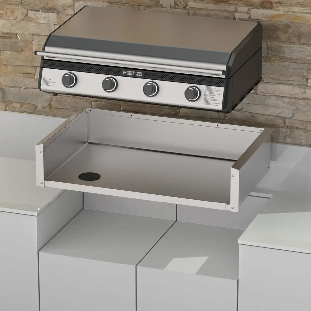 Blackstone 36-inch Drop-In Griddle positioned above the matching stainless steel insulation jacket, ready for installation in a stone outdoor kitchen setup.
