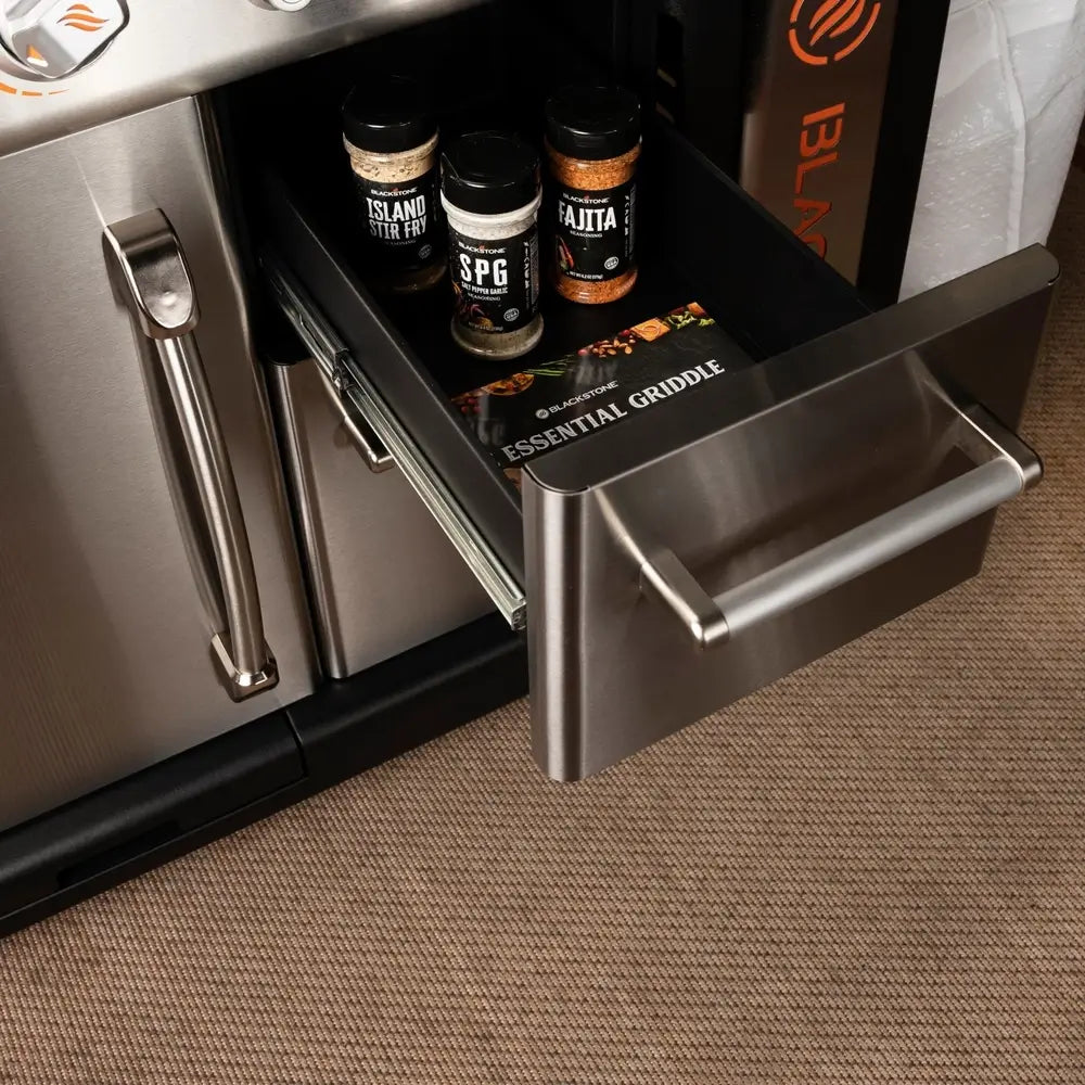 Close-up of Blackstone griddle drawer with spices and Essential Griddle Guide stored inside cabinet