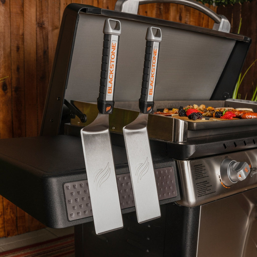 Dual Blackstone stainless steel spatulas hanging on magnetic tool bar of 36-inch griddle side shelf