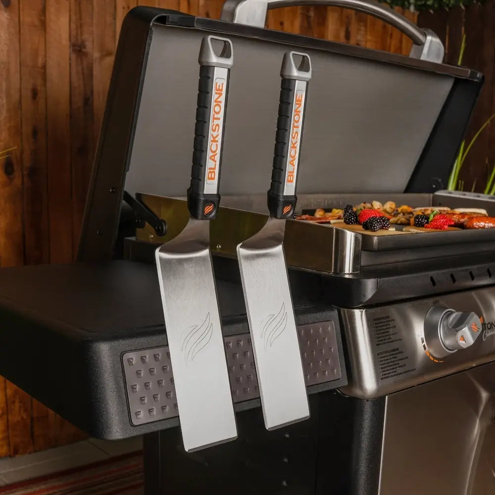 Dual Blackstone stainless steel spatulas hanging on magnetic tool bar of 36-inch griddle side shelf