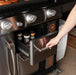 Hand opening drawer of Blackstone griddle cabinet revealing seasoning jars and stainless finish