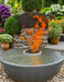 TessaRai 40-inch 360 Fire and Water Bowl with tall vibrant flames and overflowing water in a lush garden setting.