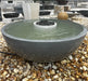 A 40-inch charcoal travertine fire water bowl filled with water on a natural stone pebble base.