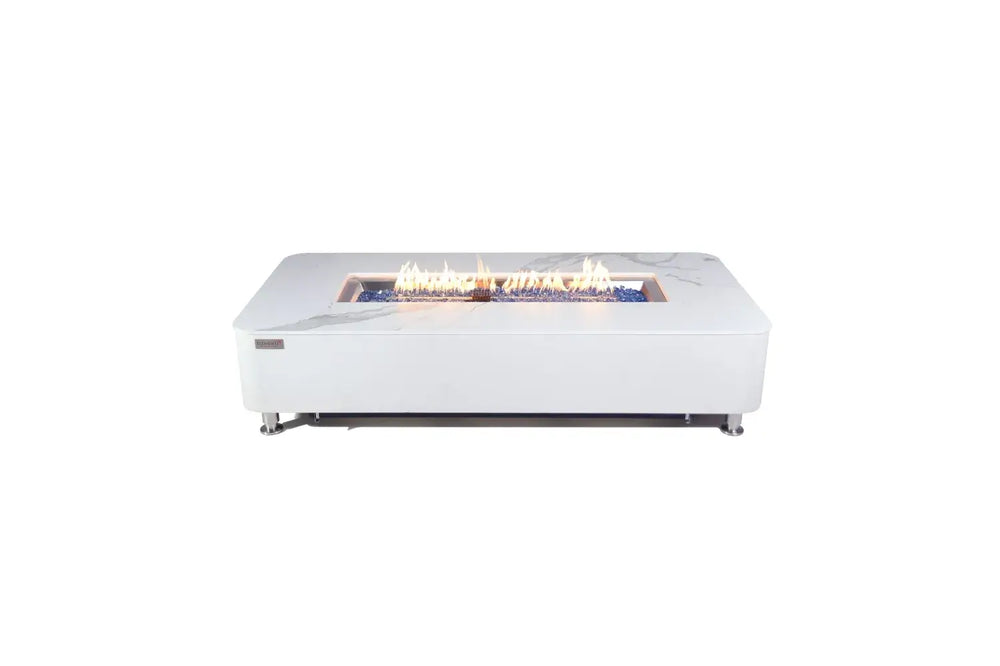 A studio shot on a plain white background showing the rectangular Athens fire table with a lit linear flame burning over a bed of vibrant blue glass rocks.
