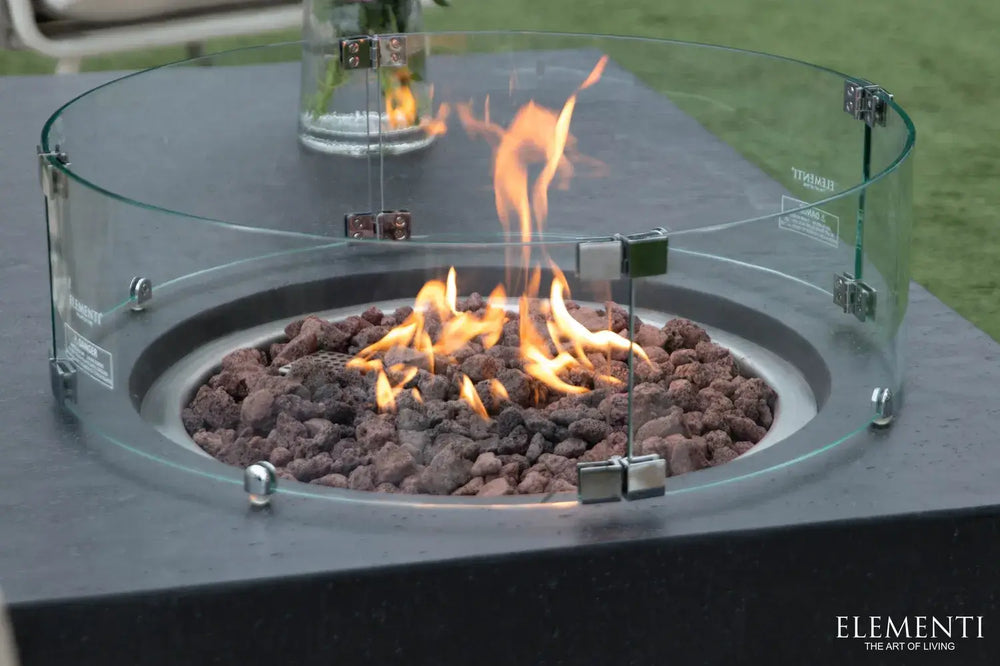 Close-up of the Metropolis fire table’s circular burner basin filled with natural lava rocks and a curved glass wind guard.
