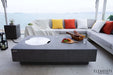 Large Elementi Metropolis fire table on a beachside patio with a curved glass wind guard and coastal views.