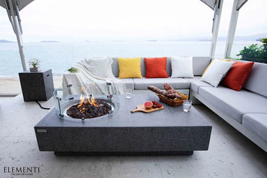 Modern patio lounge featuring a long Metropolis fire table with a circular tempered glass wind guard protecting the flames.