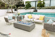 High-end backyard patio featuring the Meteora rectangular gas fire pit table as a centerpiece, paired with a designer woven chair and a classic silver trailer.
