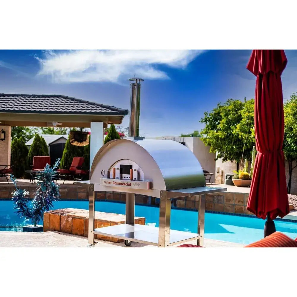 WPPO Karma 55 commercial wood-fired oven in outdoor poolside kitchen with stainless steel stand, chimney, and patio setting.