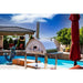 WPPO Karma 55 commercial wood-fired oven in outdoor poolside kitchen with stainless steel stand, chimney, and patio setting.