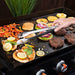 Blackstone Tongs Grabbing Chicken and Vegetables on Flat Top Grill – Premium BBQ Accessories for Griddle Enthusiasts