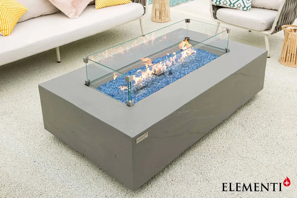 Close-up of the Meteora fire table’s linear burner, highlighting the clear tempered glass wind guard protecting a warm flame over natural lava rocks.