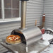 WPPO Lil Luigi portable stainless steel wood-fired pizza oven on outdoor snowy patio with pizza peel and chimney.