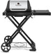 Front view of the Broil King Porta-Chef AT220 portable gas grill with stainless steel hood, black frame, folding scissor-style stand, right side shelf, and lower wire rack for propane storage.