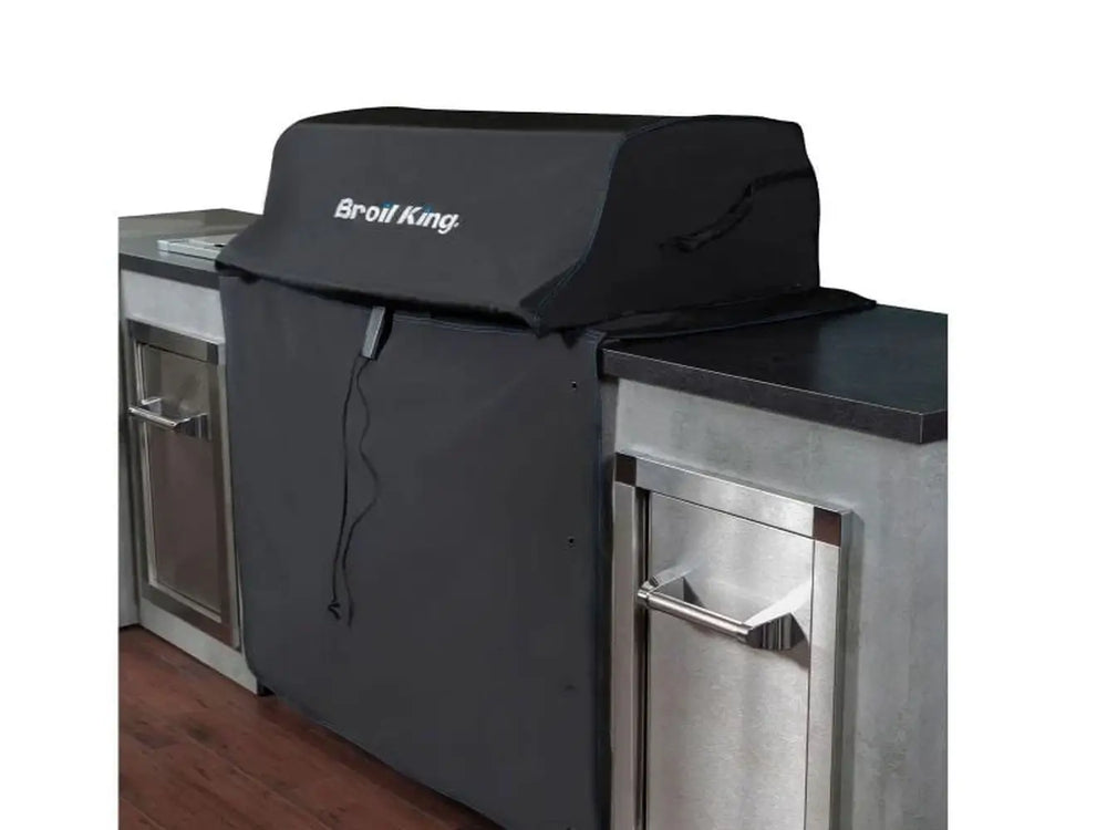 Broil King 68590 600 Series grill cover installed on a built-in grill with stainless outdoor kitchen cabinets.