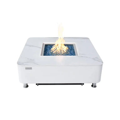 White marble Elementi Annecy 60,000 BTU fire table with a central burning flame and blue glass media.