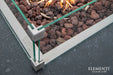 Close-up detail of the Manhattan fire table's stainless steel burner, lava rocks, and glass wind guard corner bracket.