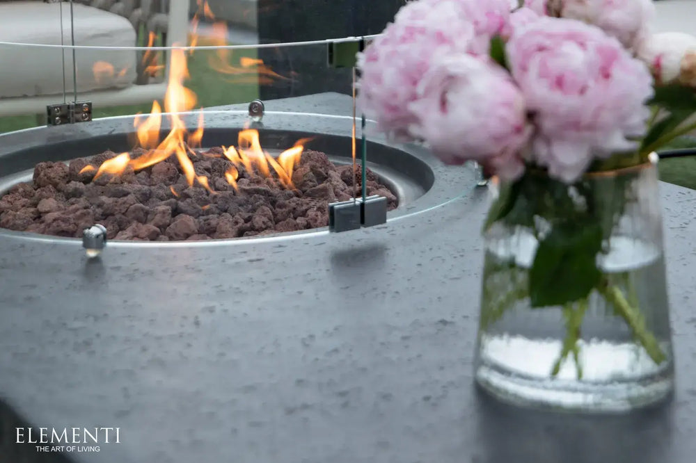 Modern outdoor living space featuring the 56-inch Metropolis fire table equipped with a protective circular glass wind guard.