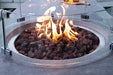 Close-up of the Metropolis fire table’s circular burner area featuring red lava rocks and a curved glass wind guard.