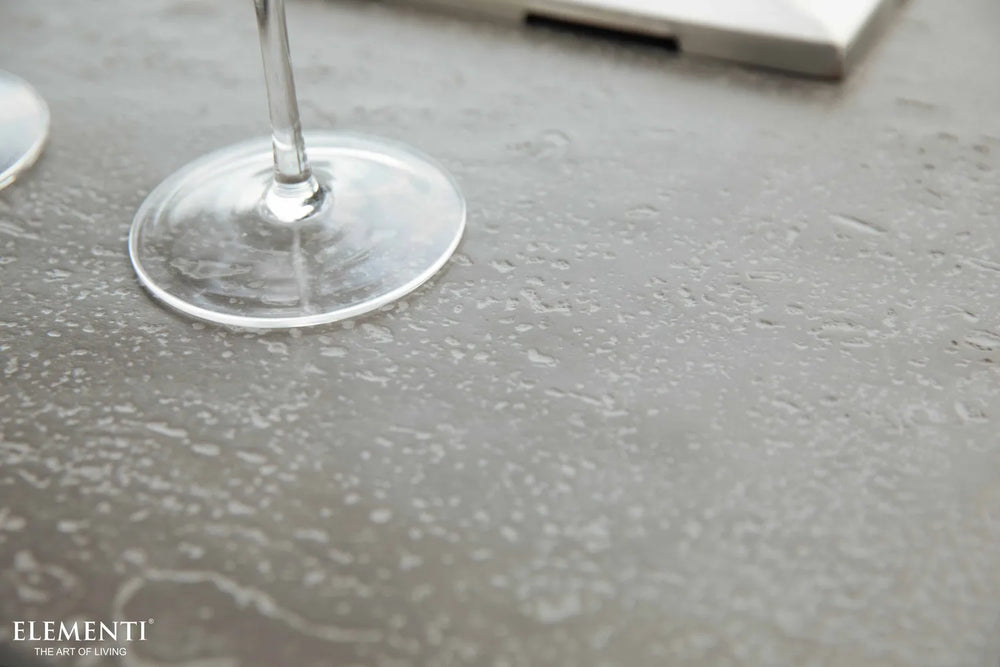 Close-up of the Elementi brand logo on the dark gray concrete-style finish of the Hampton OFG139DG Fire Table.