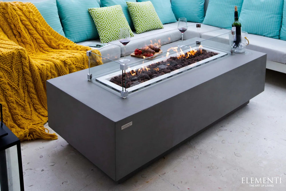 Angled view of Elementi Granville OFG121LG Fire Table with glass wind guard, wine, and appetizers.