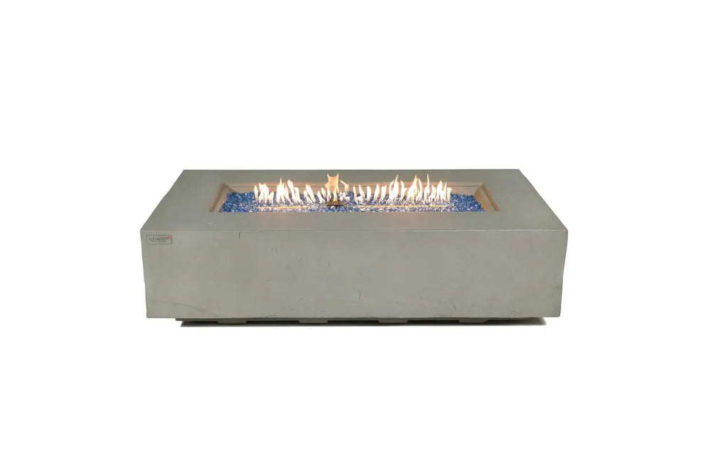 Studio product shot of the 60,000 BTU Elementi Plus Meteora fire table on a white background, featuring a lit linear flame and volcanic lava rock fire media.