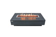 Lit Elementi Hampton OFG139DG Fire Table 56" Dark Gray with glass wind guard and lava rocks on white.