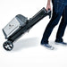 Broil King Porta-Chef AT220 portable gas grill folded into transport mode, being wheeled by a person using the integrated handle and large black wheels.