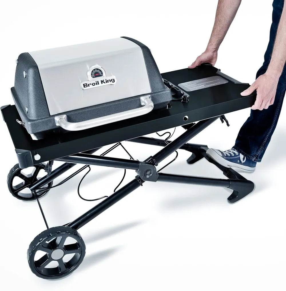 Broil King Porta-Chef AT220 portable gas grill being lowered into folded position by a person, highlighting the collapsible cart system, side shelf, and compact storage design.