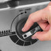 Close-up of a hand turning a Broil King Porta-Chef 320 control knob on the stainless steel panel marked “OFF / ARRÊT” and “POW-R-ZONE.”