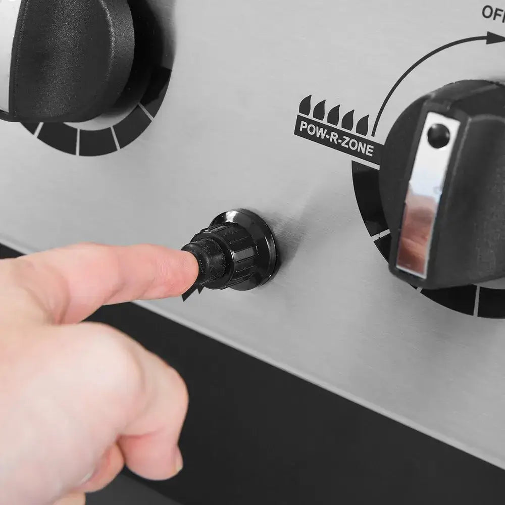 Close-up of a finger pressing the ignition button on the Broil King Porta-Chef 320 portable gas grill control panel.