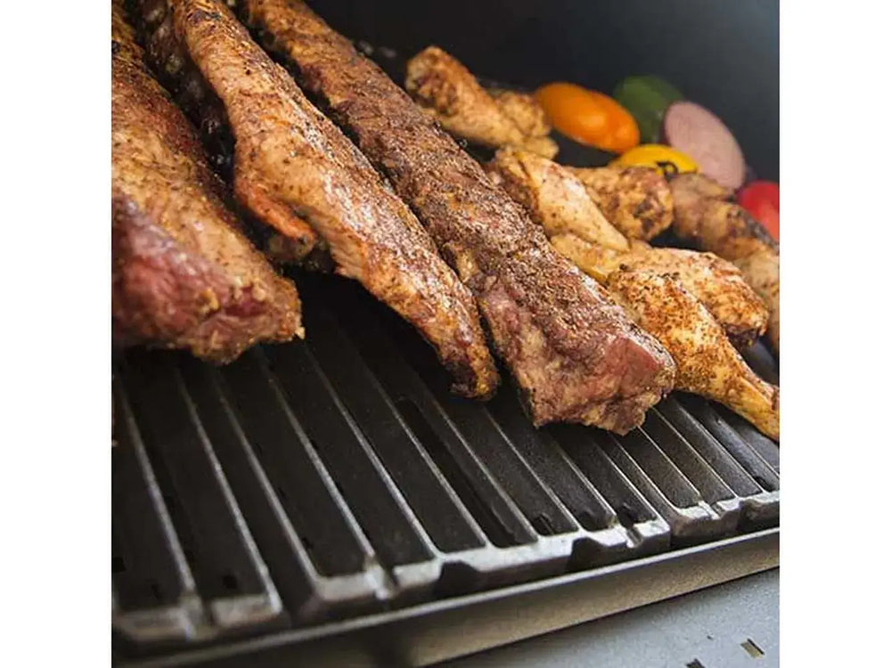 Close-up of ribs, chicken, and vegetables grilling on heavy cast iron cooking grates inside the Broil King Regal Charcoal Grill 400.