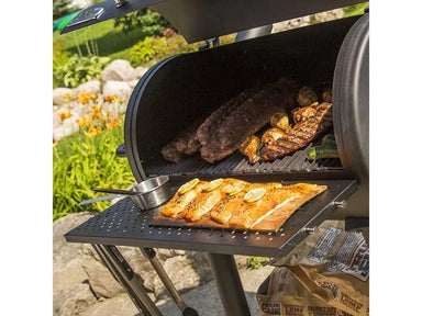 Salmon fillets on a cedar plank resting on the front shelf while meats smoke inside the Broil King Regal Charcoal Offset 400 grill.