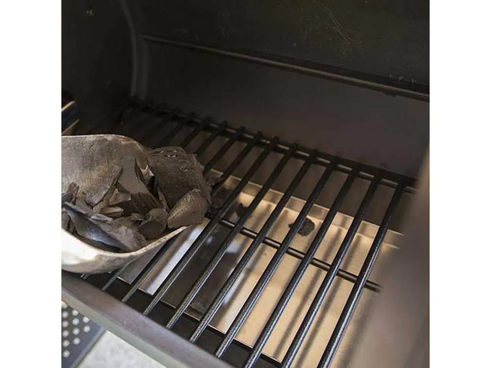 Close-up of the side firebox interior with charcoal being added to the grate inside the Broil King Regal Charcoal Offset 400 smoker grill.